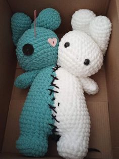 two crocheted teddy bears sitting in a cardboard box, one is blue and the other is white