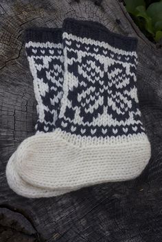 two knitted black and white socks sitting on top of a piece of tree trunk