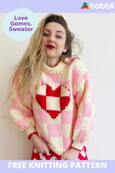 a woman wearing a pink and white knitted sweater with hearts on it, standing in front of a wall