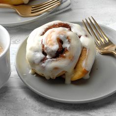 two plates with cinnamon rolls on them next to a cup of coffee and a fork