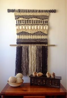 the wall hanging is made with yarn and shells on top of a wooden table in front of a white wall