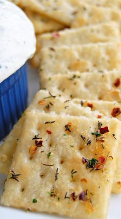 crackers are arranged on a white plate with a blue cup in the background and some herbs sprinkled on top