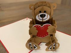 a brown teddy bear holding a heart on top of a white paper sheet with red trim