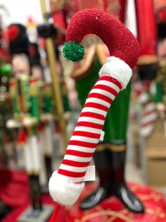 a red and white candy cane with a santa hat on it's head in front of christmas decorations