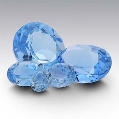 three blue gems are shown on a white surface, one is surrounded by smaller light blue stones