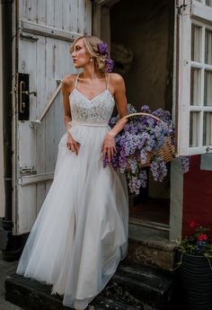 a woman in a white wedding dress standing on the steps with purple flowers behind her