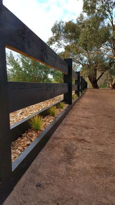 a wooden fence with plants growing in it on the side of a dirt road surrounded by trees