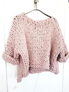 a pink knitted sweater hanging on a hanger in front of a white wall