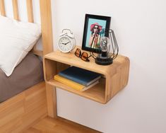 a wooden shelf with an alarm clock and some books on it next to a bed