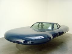 a blue car sitting on top of a cement floor next to a white wall and window