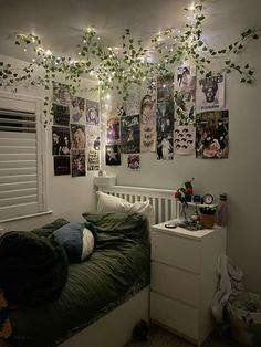 an unmade bed in a room with posters on the wall and plants hanging from the ceiling