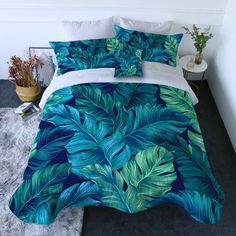 a bed with blue and green leaves on the comforter, next to a potted plant