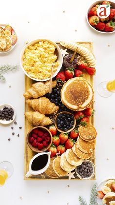 an overhead view of pancakes, fruit and other breakfast foods on a wooden platter