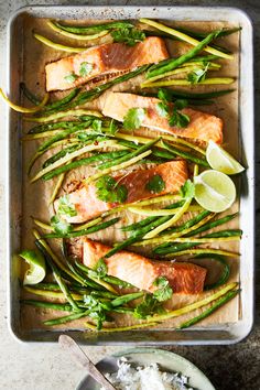 salmon and asparagus on a baking sheet with lime wedges, rice and cilantro