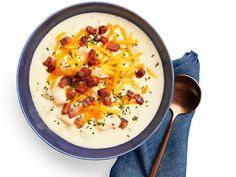 a bowl of potato soup with bacon and cheese on top, next to a spoon