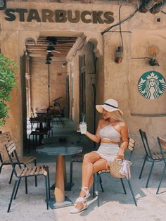 a woman sitting at a table with a starbucks cup in her hand and a straw hat on her head