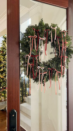 a wreath hanging on the front door of a house with ribbon tied around it's edges