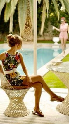 a woman sitting on top of a chair next to a table near a swimming pool