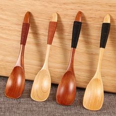 four wooden spoons lined up in a row on a table next to a wall