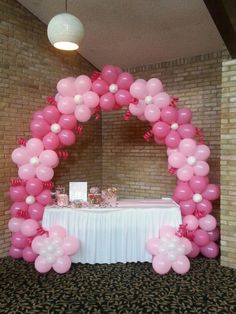 a table topped with pink balloons next to a white table cloth covered table and brick wall