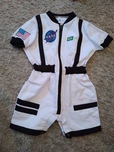 a white and black astronaut romper with patches on the chest is laying on carpet