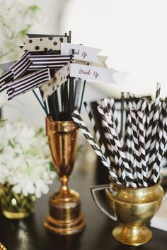 black and white striped paper straws in gold cups on a table next to flowers