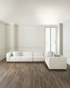 a white couch sitting on top of a hard wood floor next to a large window