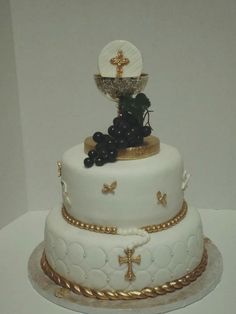 a three tiered cake with grapes on top and a cross on the side,