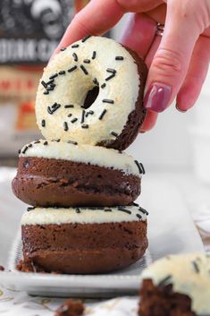 a hand is holding a chocolate donut with white frosting and sprinkles