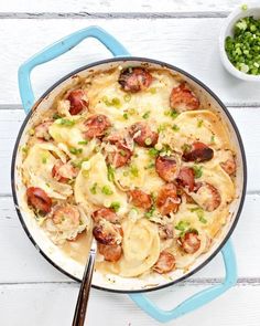 a skillet filled with pasta and sausage on top of a white table next to peas