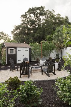 an outdoor patio with chairs, table and shed in the back ground area next to trees