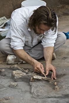 a man kneeling down on the ground working on something in front of him with his hands