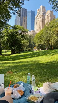 a picnic table with food and drinks on it in the middle of a city park