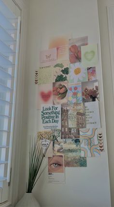 a white vase with a plant on top of it next to a wall covered in pictures