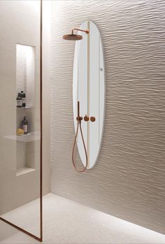 an oval mirror hangs on the wall next to a shower head and faucet