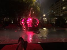 a person's feet resting on the edge of a fountain at night