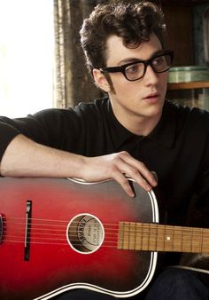 a young man with glasses holding a red guitar