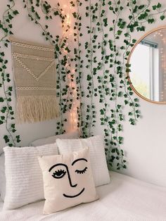 a white bed topped with pillows next to a wall covered in green plants and lights