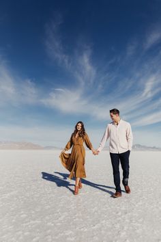 a man and woman holding hands in the middle of an empty desert with blue skies