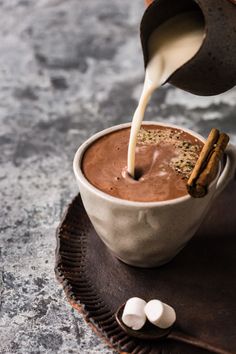 a person pouring milk into a cup filled with hot chocolate