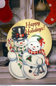 a couple of snowmen standing next to each other in front of a christmas sign