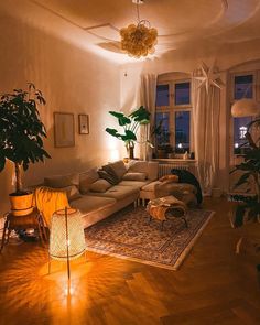 a living room filled with lots of furniture and plants on top of a hard wood floor