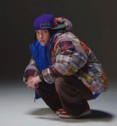 a young man squatting on the ground with his skateboard in hand and wearing a purple hat