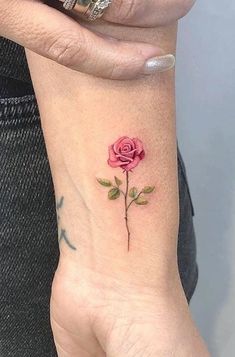 a woman's wrist with a pink rose tattoo on the left side of her arm