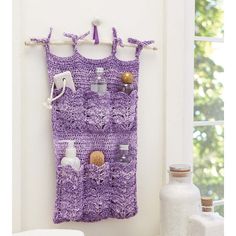 a purple crocheted purse hanging on a wall next to a bottle and vase