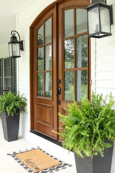 two large planters with plants on the front porch next to an entryway door