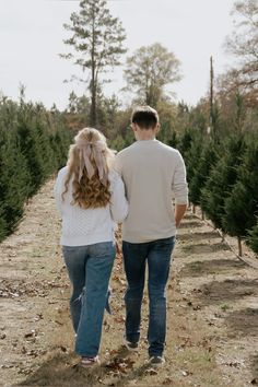 a man and woman walking down a tree farm holding hands