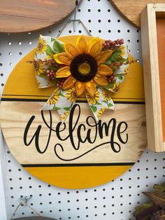 a welcome sign with sunflowers and leaves on it hanging from a wall next to other items