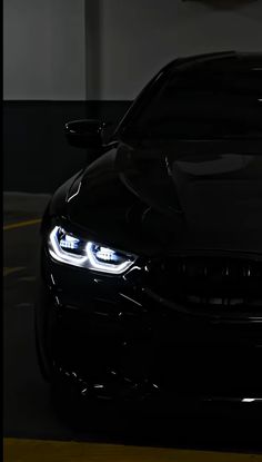 the front end of a black car with its lights on