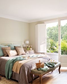 a bed sitting in a bedroom next to a window with lots of pillows on top of it